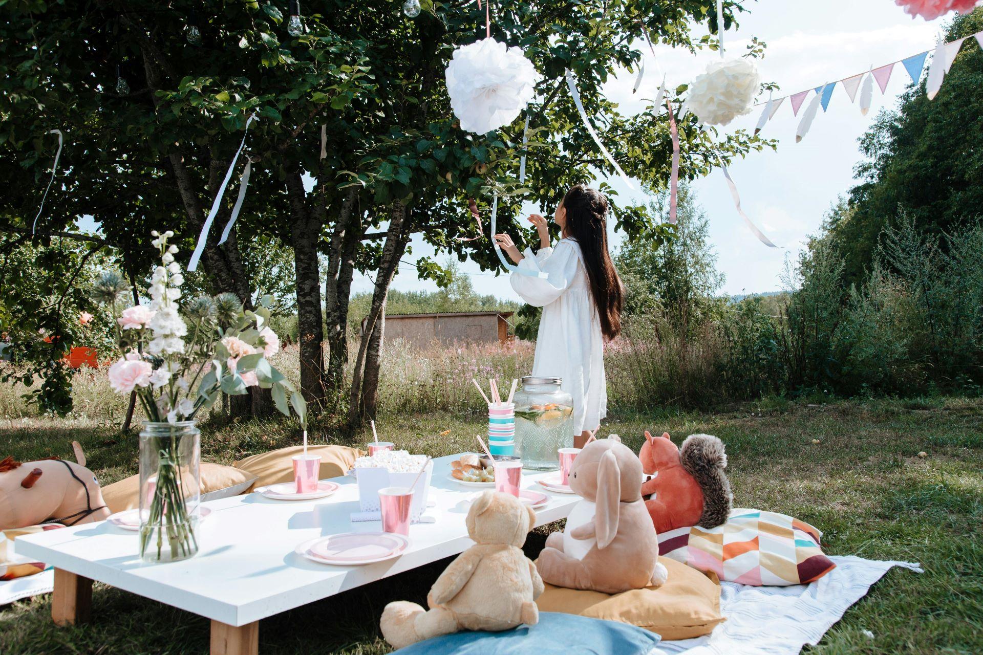 Ein dekorierter Gartentisch mit Blumen und bunten Kissen, ein perfekter Ort für ein Picknick im Grünen, mit einer Frau im Hintergrund.