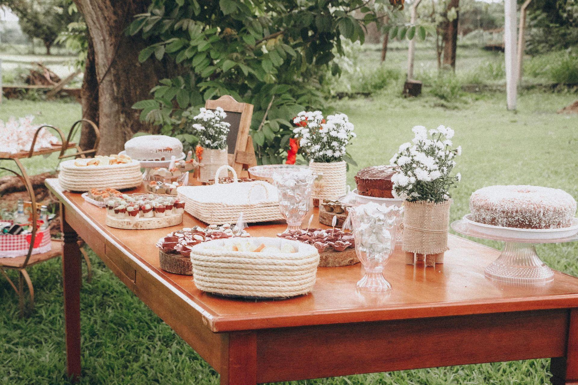 Ein großer Holztisch im Garten, dekoriert mit Blumen, Kuchen und Desserts, perfekt für ein Outdoor-Gartenbuffet.