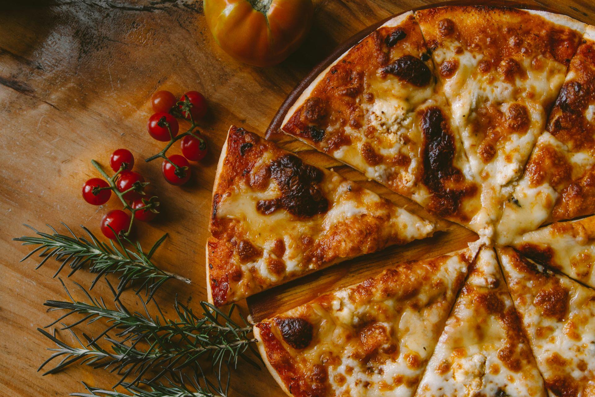 Frisch gebackene Pizza mit Tomaten, Rosmarin und rustikalem Holzbrett als Unterlage