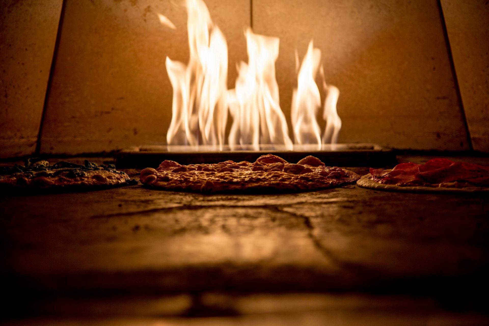 Pizzaofen mit brennendem Holz und knusprigen Pizzen im Vordergrund