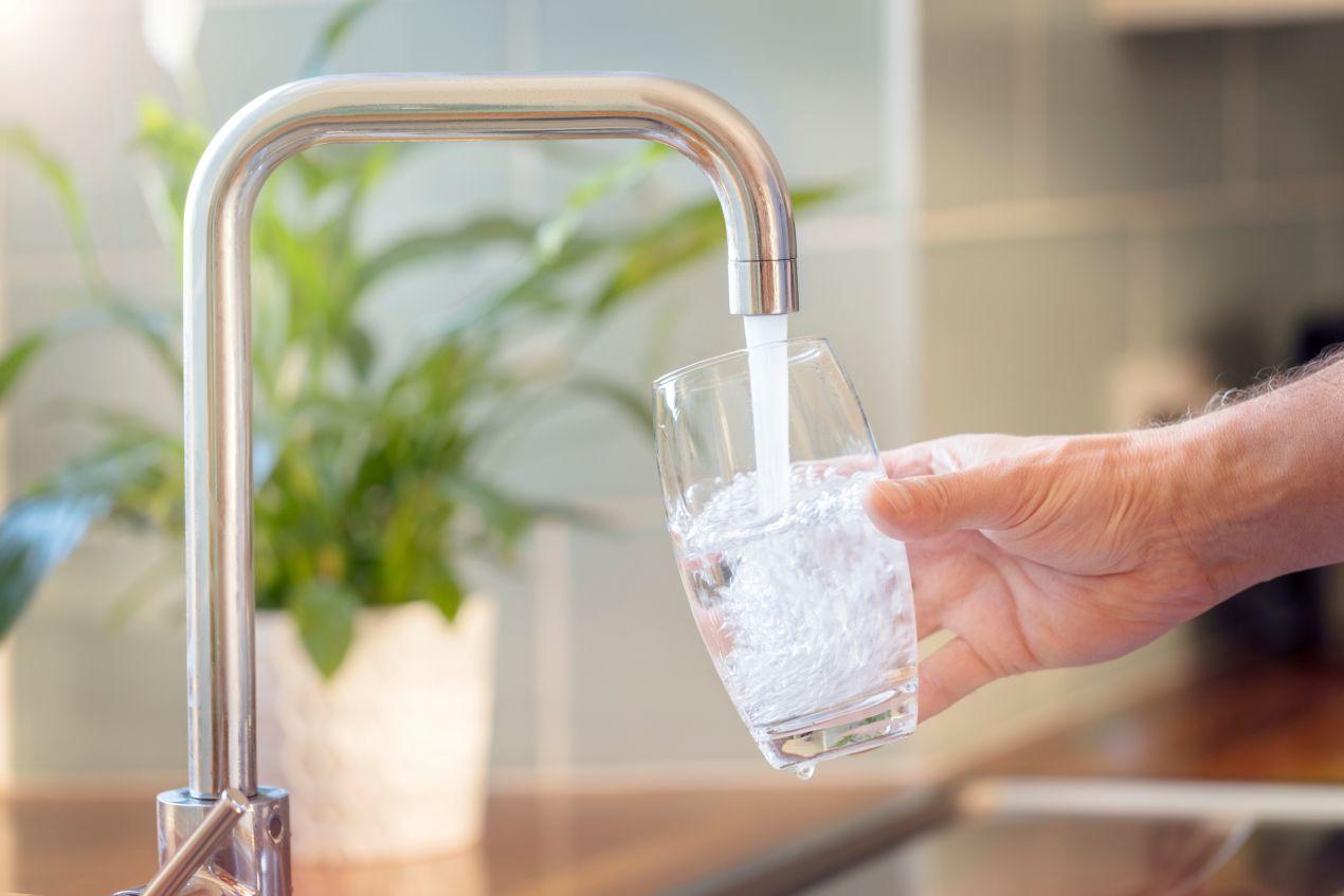Hand hält ein Glas unter Wasserhahn mit klarem Leitungswasser dank moderner Entkalkungsanlagen in der Küche