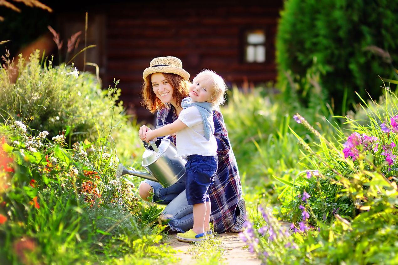 Umweltstrafrecht im Familiengarten – Mutter und Kind giessen gemeinsam Blumen im naturnahen Vorgarten