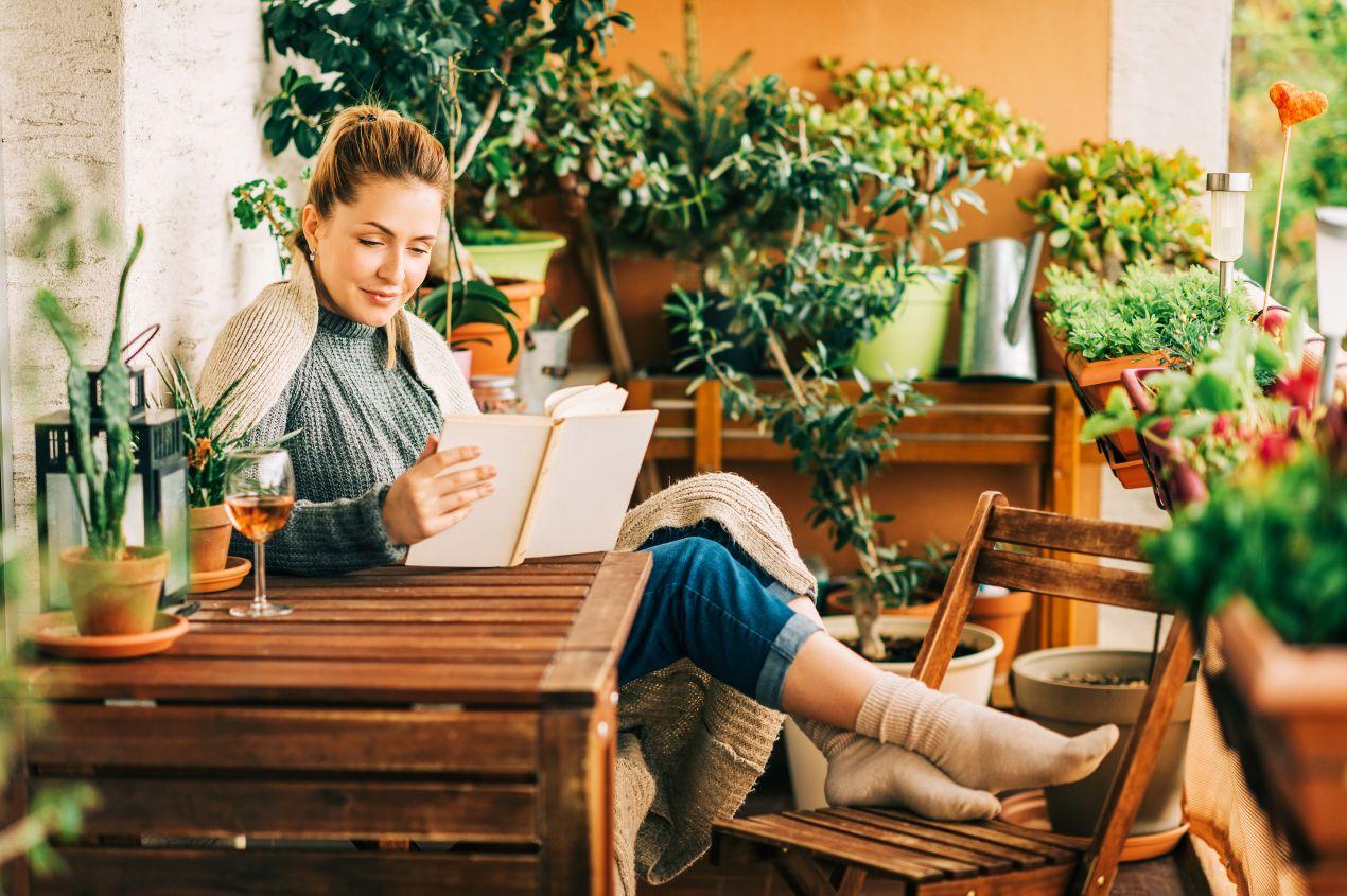 Frau mit Buch und Glas Wein auf einem herbstlich bepflanzten Balkon mit vielen Kraeutern – ein Beispiel fuer Balkonpflanzen für jede Jahreszeit